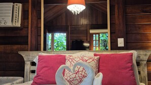 A wooden cabin room with a bed, a chandelier, and a large mirror reflecting the outside view. - Aratinga inn (Angra dos Reis)