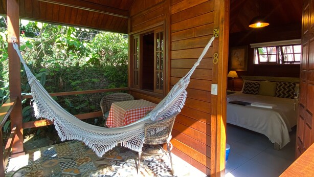 A wooden cabin with a hammock, a bed, and a tiled patio area. - Aratinga inn (Angra dos Reis)