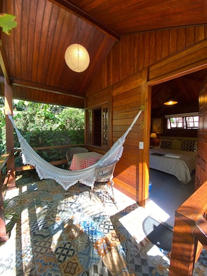 A wooden cabin with a hammock, a bed, and a tiled patio area. - Aratinga inn (Angra dos Reis)