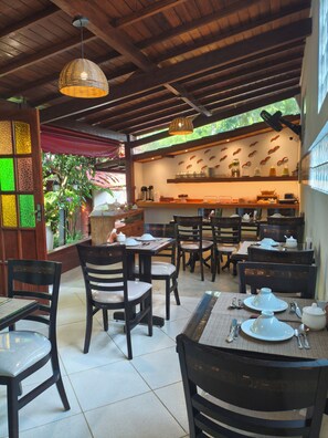 A restaurant with wooden furniture, a tiled floor, and a kitchen area with shelves. - Aratinga inn (Angra dos Reis)