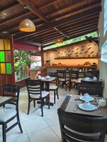Un restaurante con mobiliario de madera, piso de baldosas y una zona de cocina con estanterías.