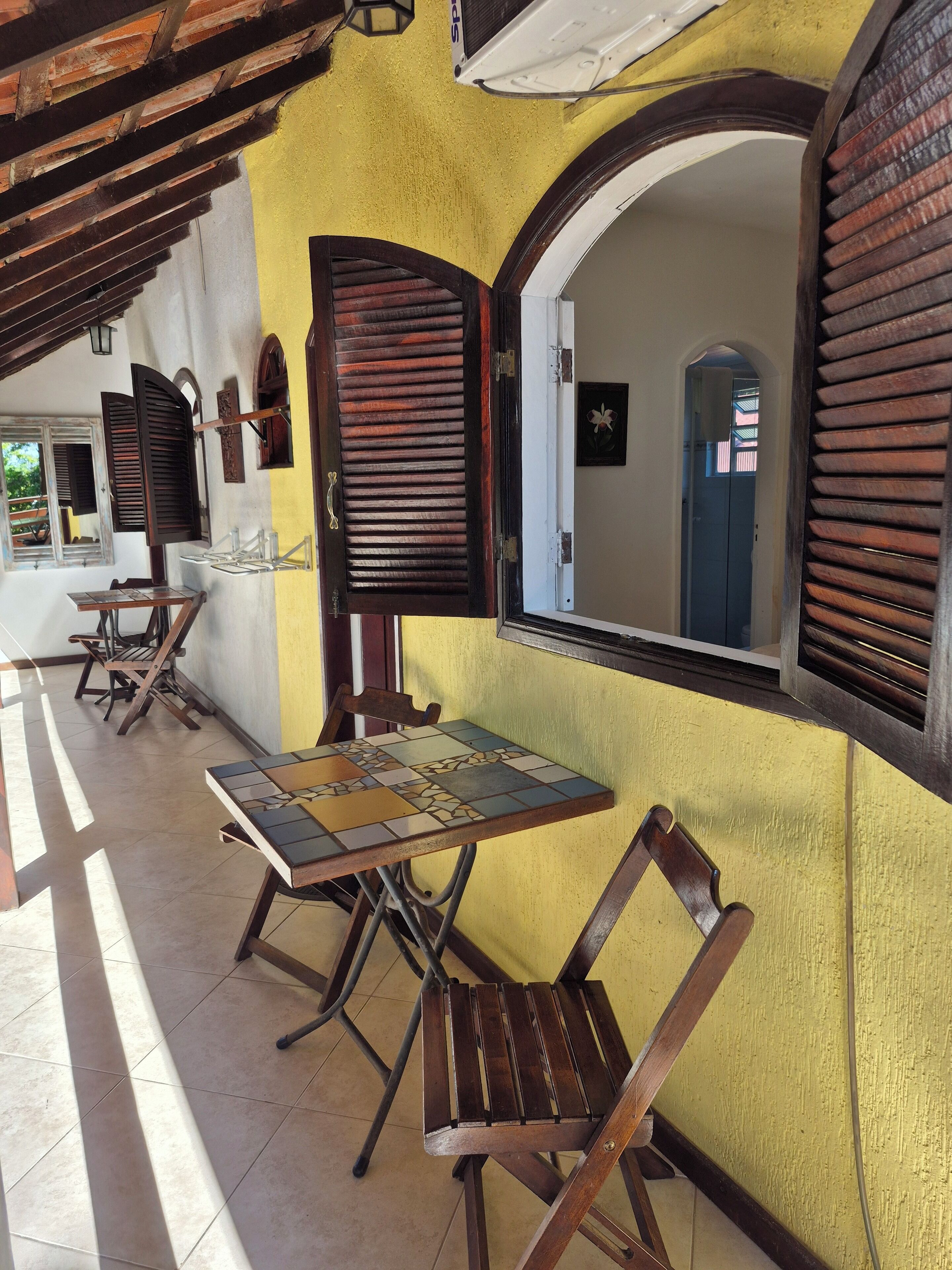 Un espacio de descanso al aire libre cubierto, con mobiliario de madera y suelo de baldosas.