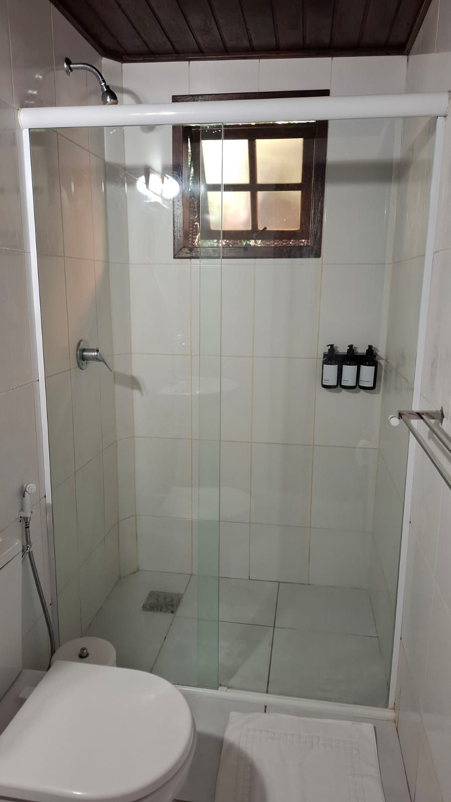 Une salle de bain avec une douche à parois de verre, des toilettes et une petite fenêtre située au-dessus de la douche.