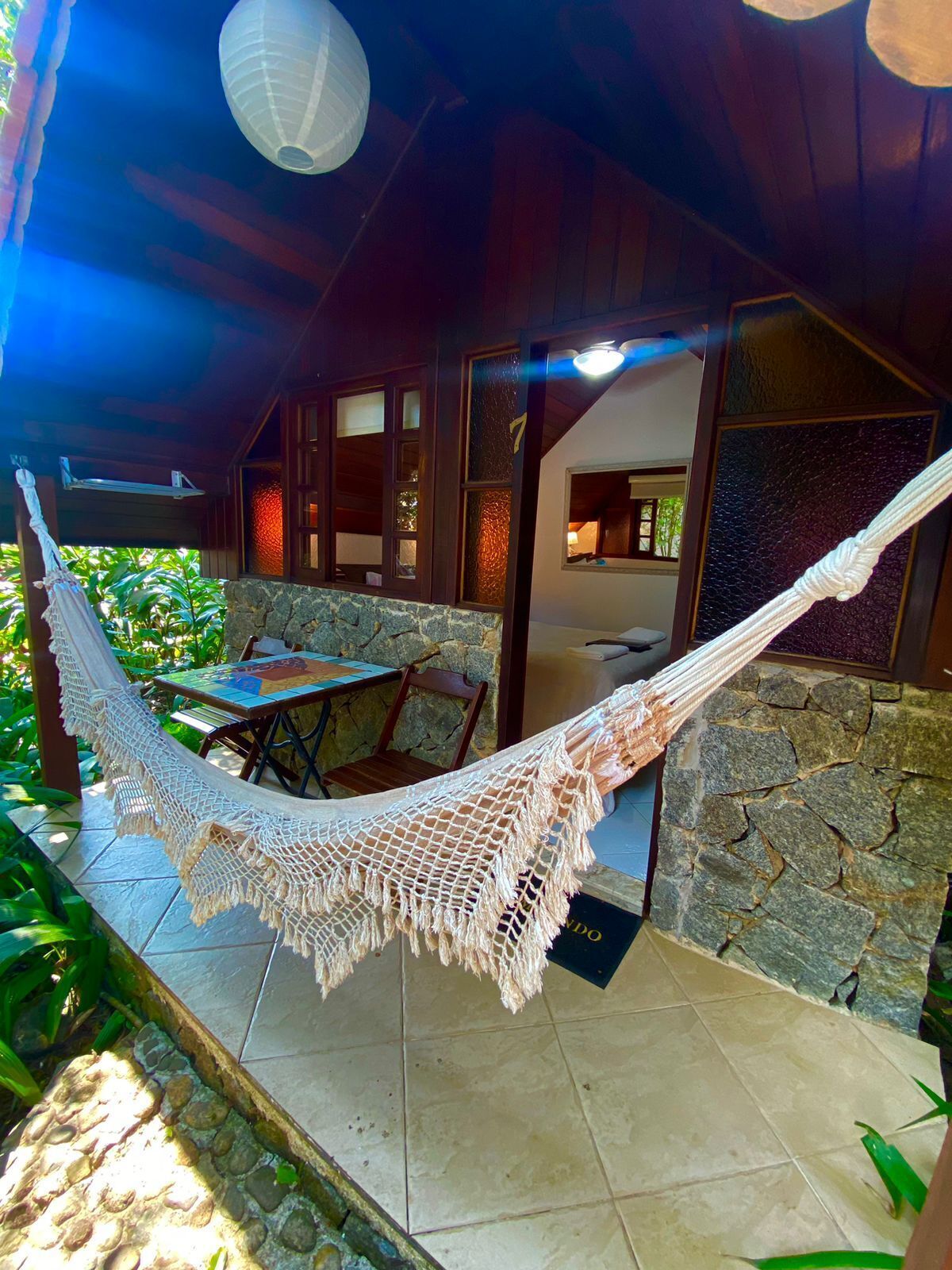 A hammock under a wooden ceiling, a stone wall, a tiled patio, and a door with a number.