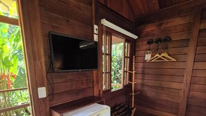 A wooden room with a television mounted on the wall, a refrigerator, and a window with wooden shutters. - Aratinga inn (Angra dos Reis)