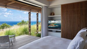 Ein Schlafzimmer mit einem großen Bett, einem Fernseher auf einer Holzregal und Blick auf den Ozean.