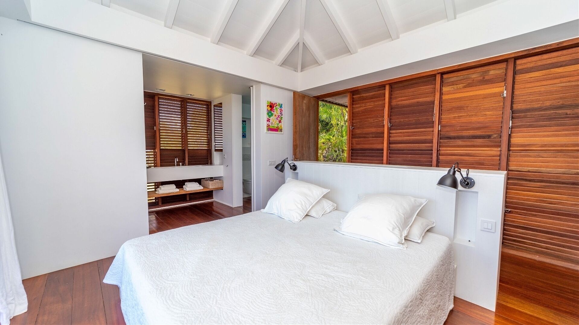 A bedroom with a large bed, wooden shutters, and a view of greenery outside.