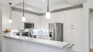 A modern kitchen with white cabinetry, stainless steel appliances, and pendant lighting. - Private Mauna Lani Residence with Pool (Kamuela)