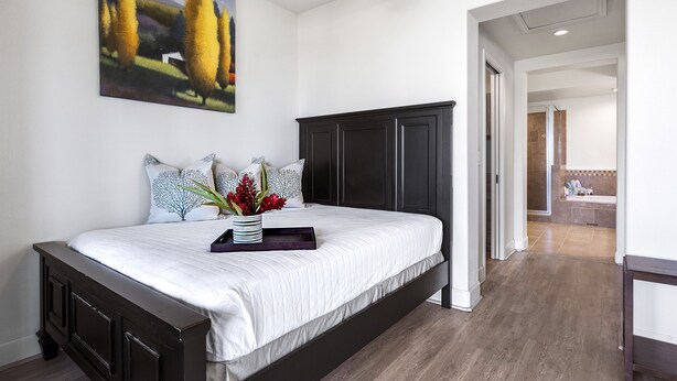 A bedroom with a large bed, dark headboard, white bedding, and a painting on the wall.