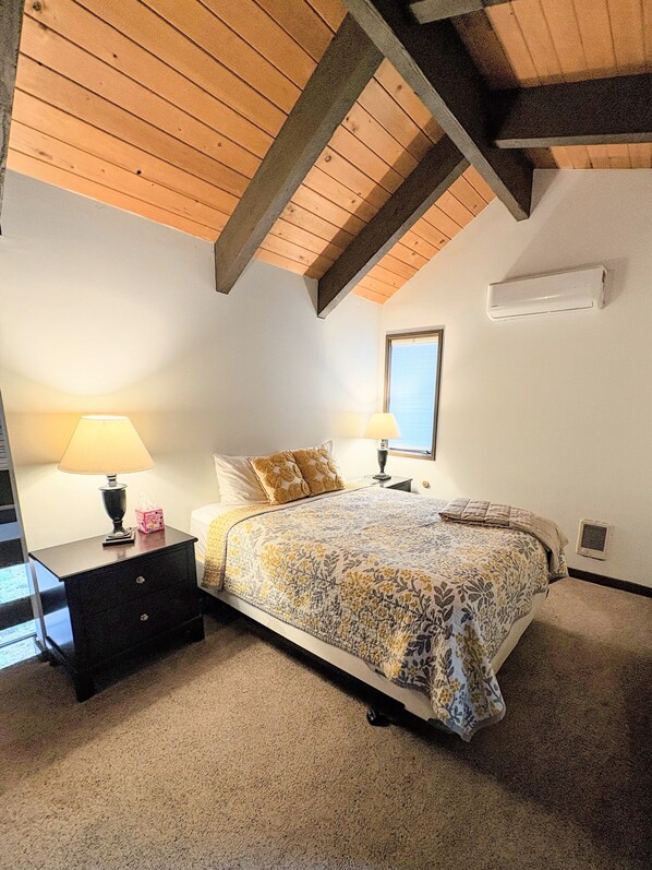 Une chambre à coucher comprenant un lit, deux tables de chevet, une lampe, une fenêtre et un plafond avec des poutres apparentes.