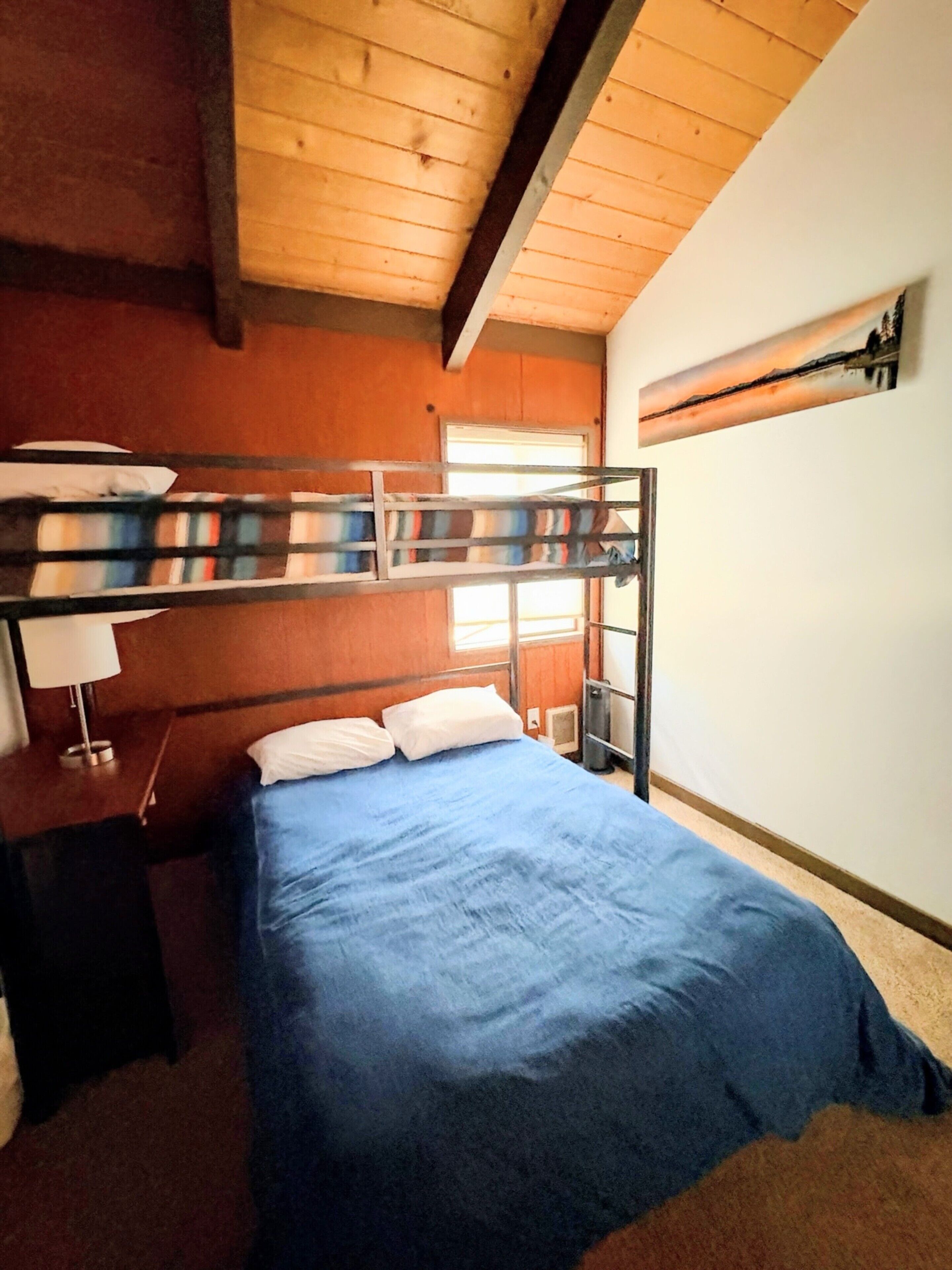 Une chambre avec un lit superposé, un bureau et une lampe, des murs en bois et un tableau accroché au mur.