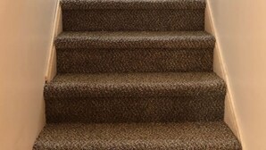 Una escalera alfombrada con barandillas de madera y una pared de color claro.