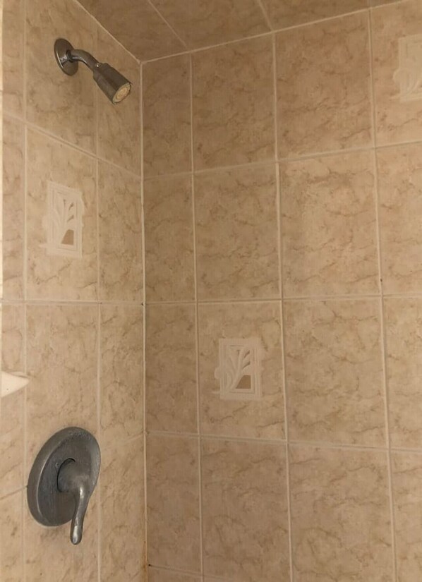 A corner shower with beige tiles and a wall-mounted showerhead.