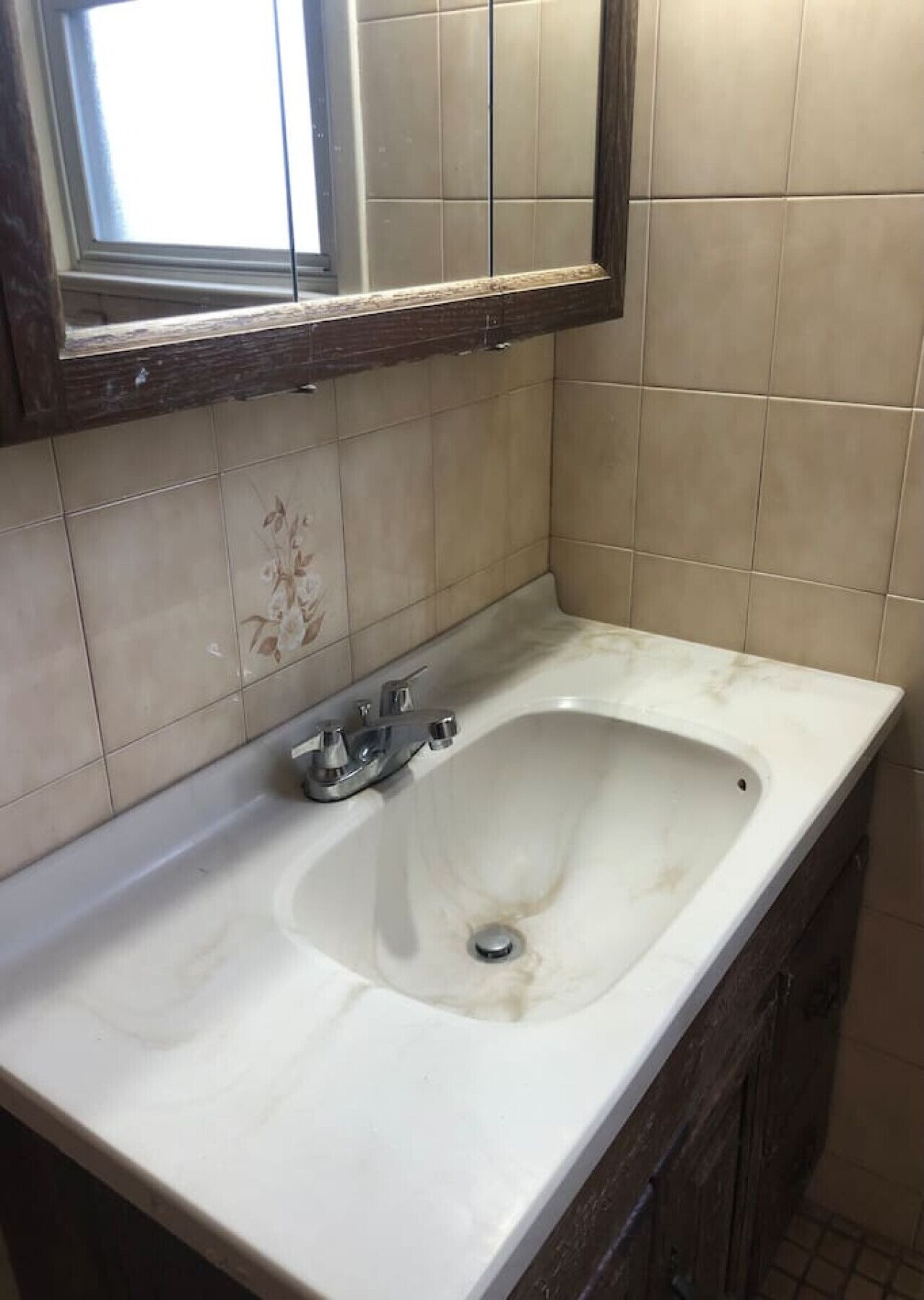 Une salle de bain avec un lavabo blanc, un miroir au-dessus et des murs recouverts de carreaux beiges.