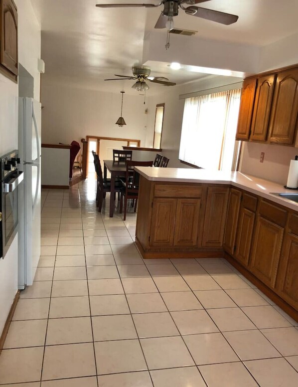 A spacious kitchen with wooden cabinets, a dining area with chairs, and a ceiling fan.