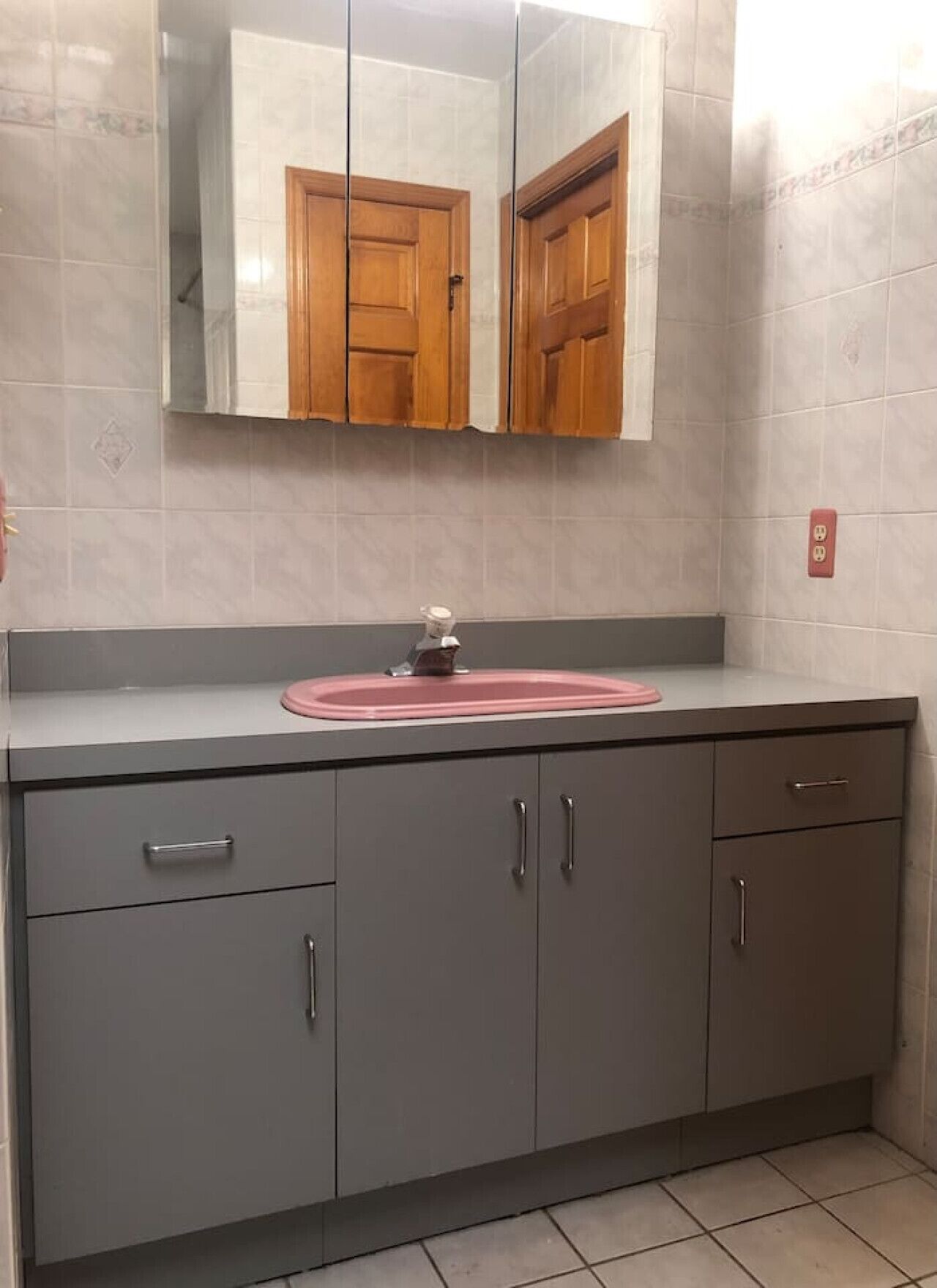 Un bagno con un vanità grigio, un lavandino rosa e uno specchio sopra il mobile contenitore.
