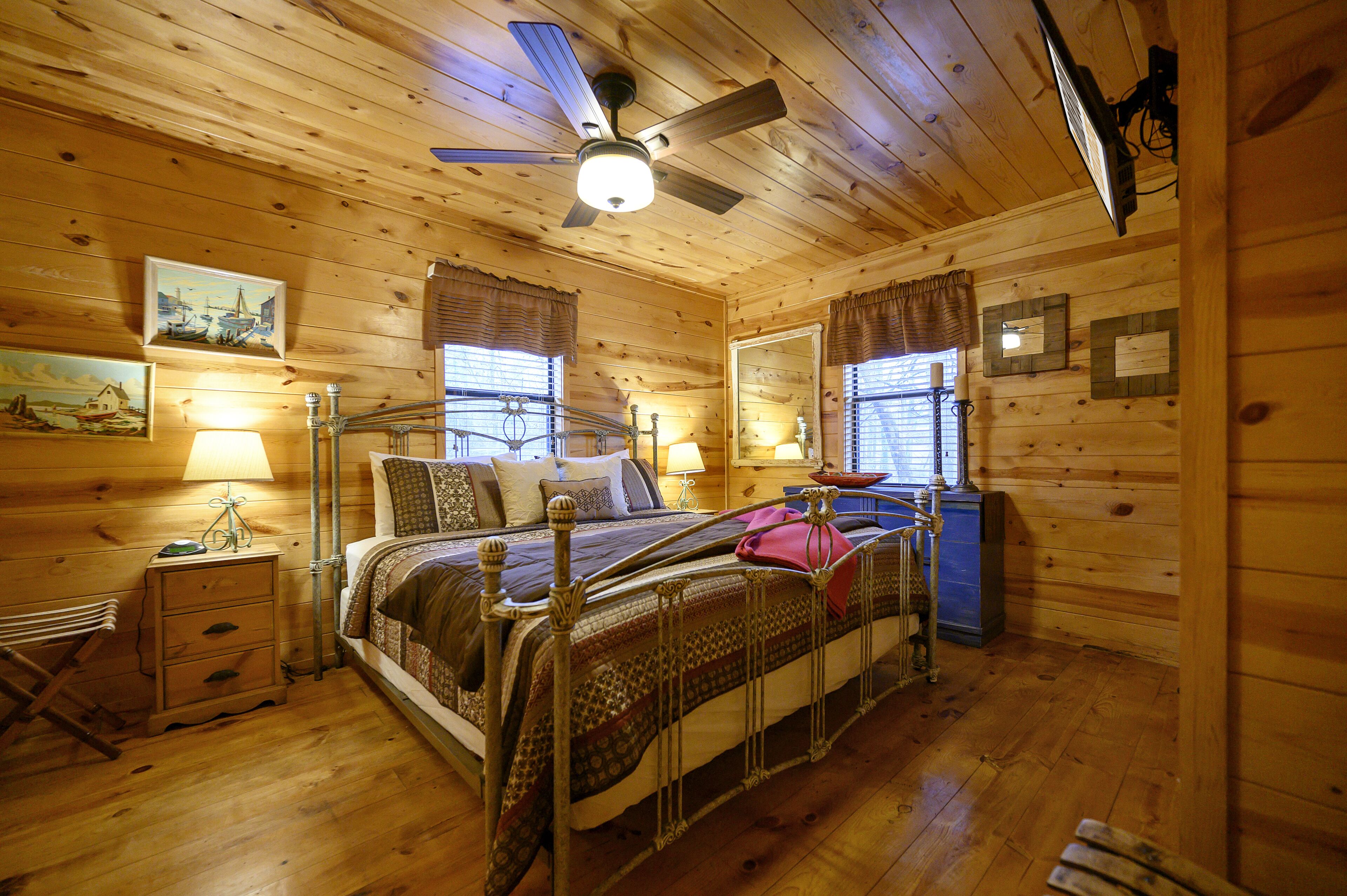 Ein Schlafzimmer in einer Holzhütte mit einem Bett, Nachttischlampen, einem Deckenventilator und einer Kommode.