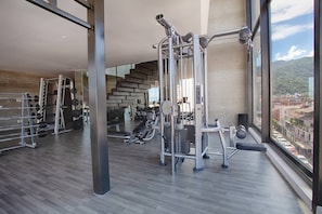 Een moderne sportschool met diverse fitnessapparaten, een trap en een groot raam met uitzicht op de stad.