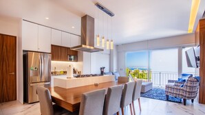 A modern kitchen with a central island, stainless steel appliances, and a dining area with a large table and chairs. - Stylish 2BR w/ View & Gym in Romantic Zone (Puerto Vallarta)