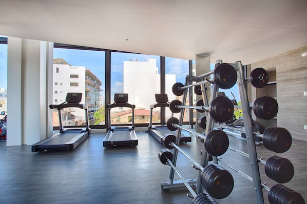 A gym with treadmills, a weight rack, and large windows overlooking a cityscape.
