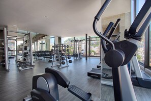 A modern gym with various exercise equipment, large windows, and a view of the city.