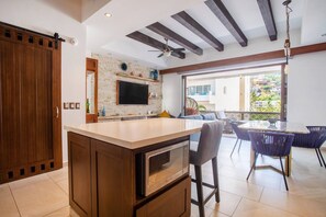 A modern kitchen with a central island, a dining area with a glass table, and a view of the outside. - Workspace, Mini-Bar & Rooftop Pool | 2BR Retreat (Puerto Vallarta)