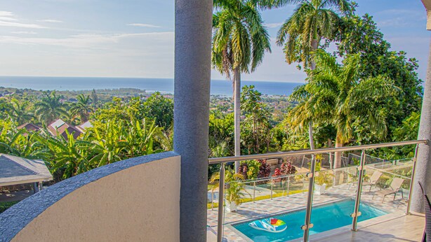 Área da piscina com vista para o oceano e vegetação ao redor.