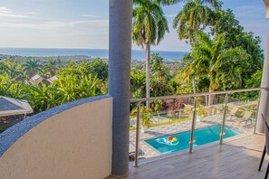 A pool area with a view of the ocean and surrounding greenery.