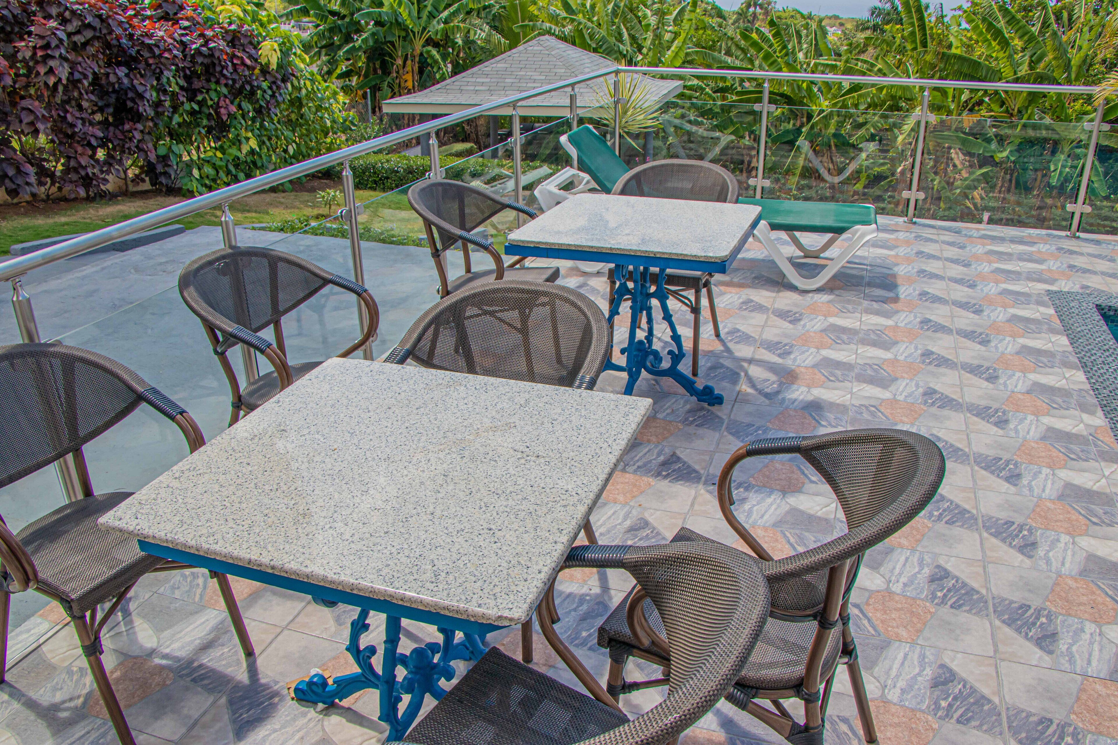 Eine Terrasse im Freien mit Tisch und Stühlen, umgeben von einem Glasgeländer und üppiger Bepflanzung.