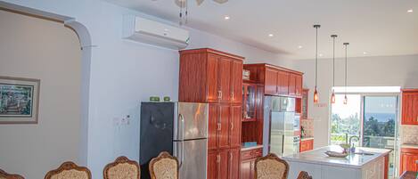 A modern kitchen with wooden cabinets, a stainless steel refrigerator, and a dining area with a table and chairs.