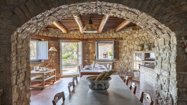 Uma sala de jantar rústica com um arco de pedra, uma mesa grande e um candeeiro rústico.