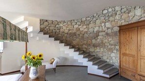 Uma escadaria com parede de pedra, uma cadeira branca e um armário de madeira.