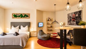 A modern hotel room with a bed, a desk, a chair, a red rug, a bookshelf, and a wall-mounted TV.