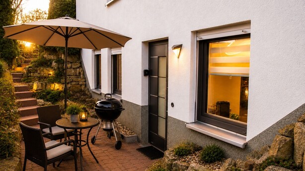 An outdoor patio with a grill, chairs, and an umbrella.