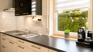 A modern kitchen with a sink, dishwasher, and a window with a view of greenery.