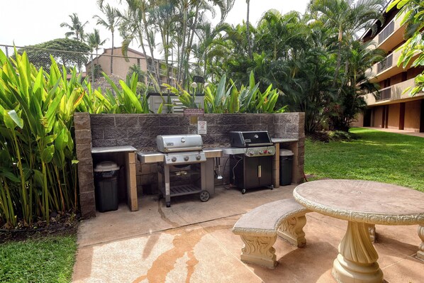 An outdoor barbecue area with a grill, a trash bin, and a table.