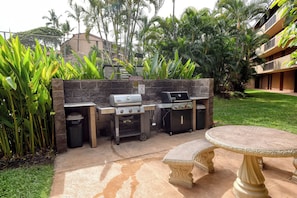 Un espace barbecue extérieur comprenant un gril, une poubelle et une table.