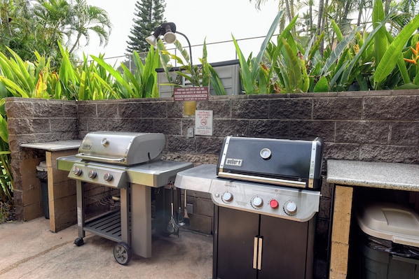 Two Weber Genesis gas grills with a stone wall backdrop, a trash can, and a sign prohibiting smoking. - The Ultimate Escape. Relax, Enjoy, Steps to Beach (Kihei)