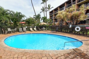 A swimming pool with lounge chairs and a fence, surrounded by palm trees and a building.