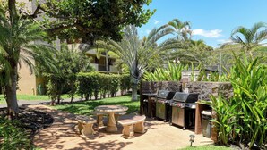 An outdoor patio with a barbecue grill, stone tables, and lush greenery.