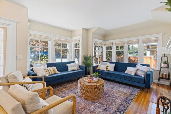 A living room with two blue sofas, a wicker coffee table, and a patterned rug.