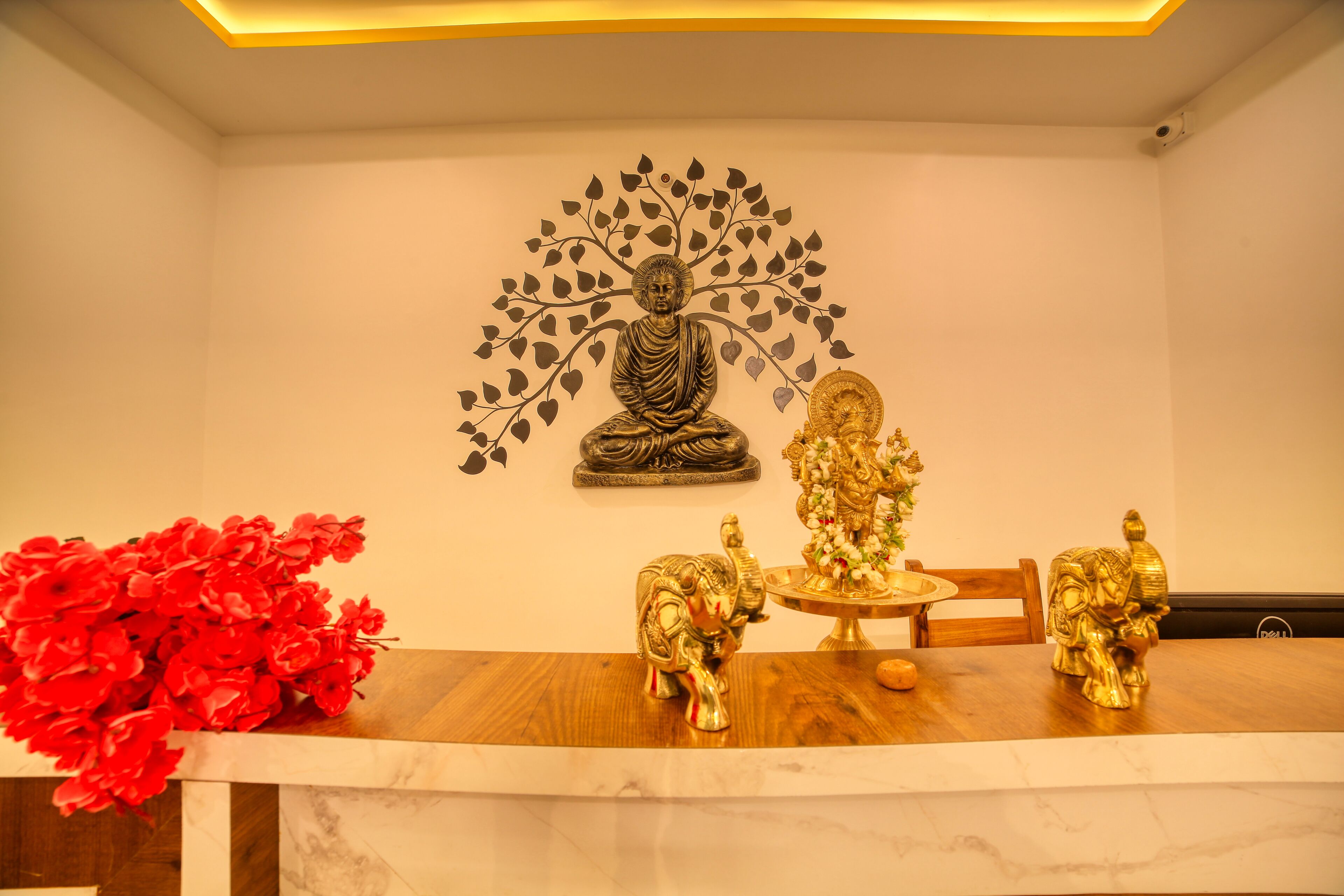 Une pièce avec une table en bois, une statue de Bouddha et une fresque représentant un arbre sur le mur.