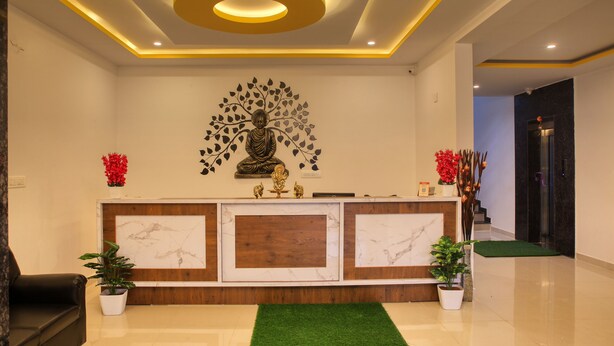 A reception area with a marble and wood reception desk, a Buddha statue, potted plants, and a green carpet. - Visa Inn Bangalore Airport (Bengaluru)