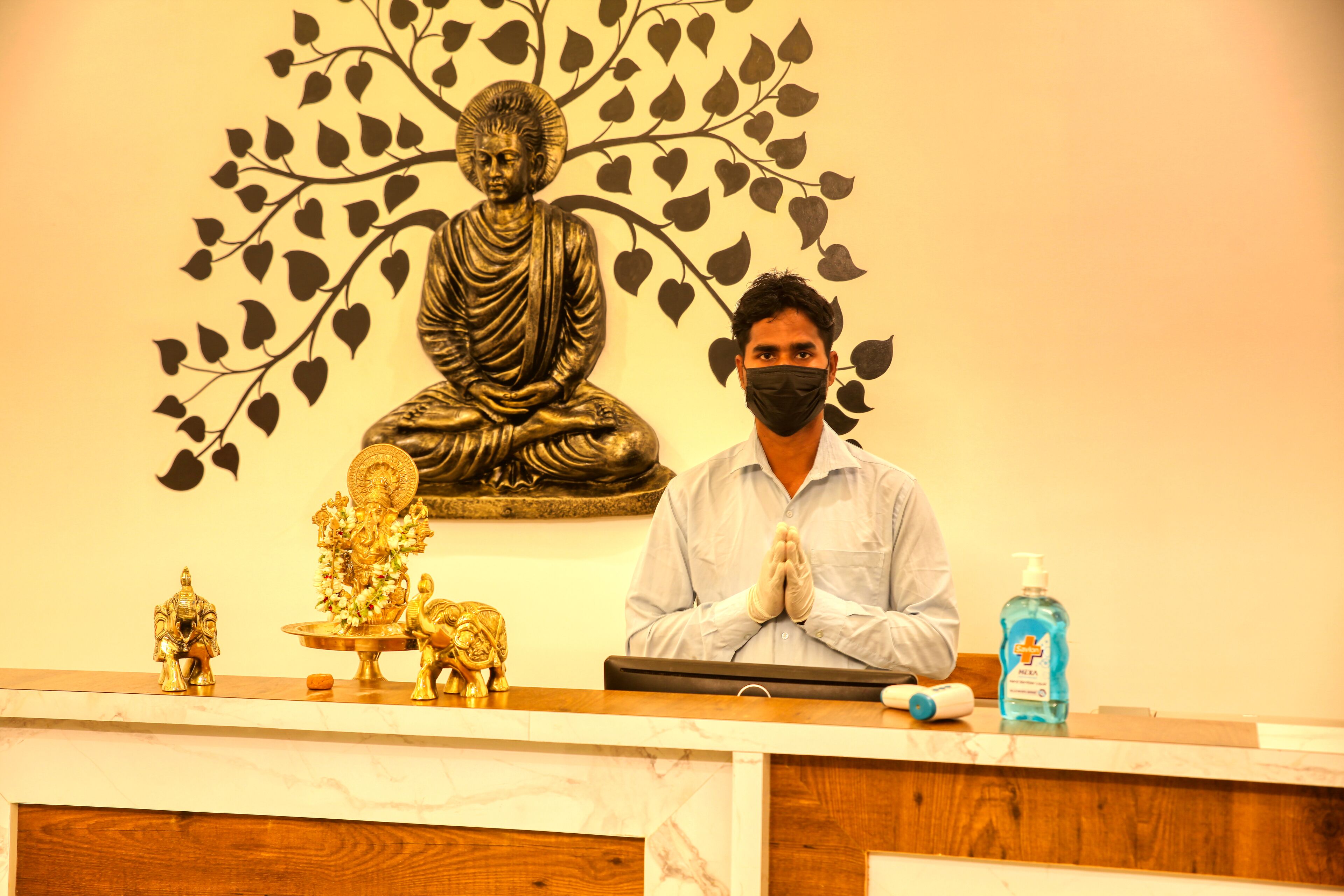 A reception desk with a Buddha statue, a small elephant statue, and a decorative tree mural in the background.