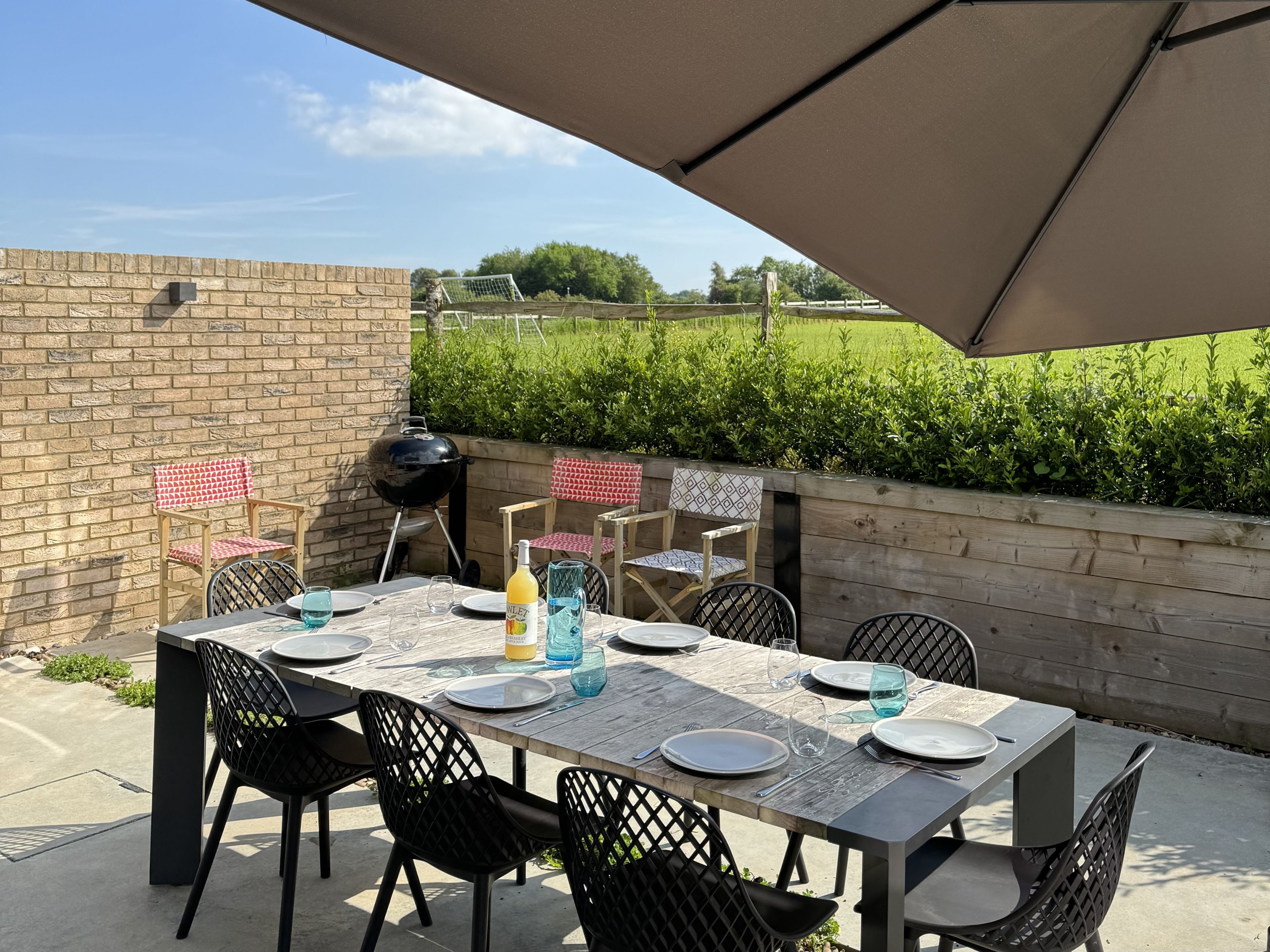 An outdoor patio with a table set for four, surrounded by chairs, a grill, and a brick wall.