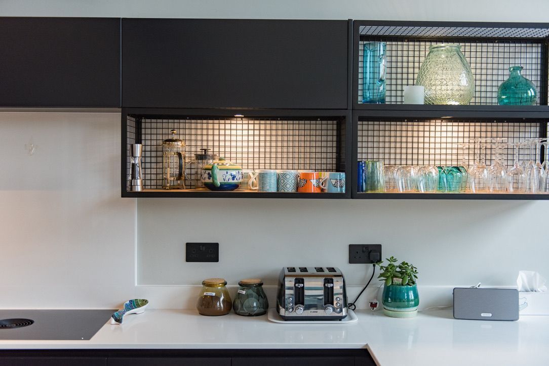 A kitchen with black cabinets, a white countertop, and shelves with glassware and jars.