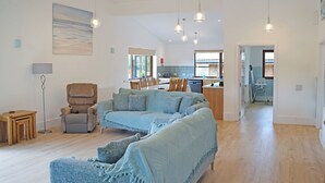 A spacious living area with a large sofa, a dining table, and a kitchen in the background. - 3 bedroom accommodation in Llandrindod Wells (Llandrindod Wells)