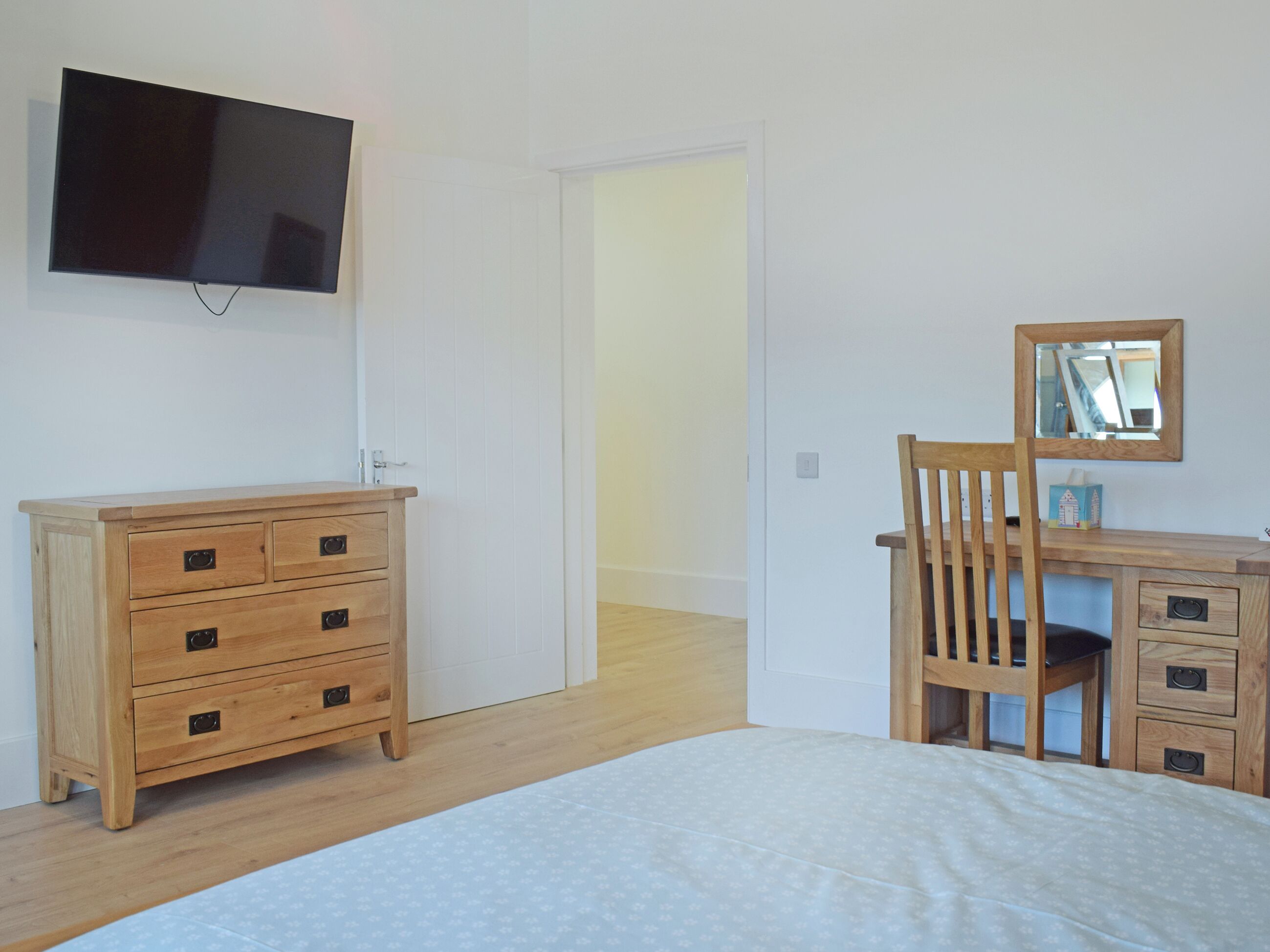 Une chambre à coucher avec un lit, une commode en bois et un bureau doté d’un miroir.