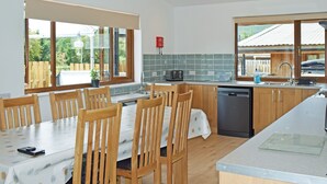 A modern kitchen with wooden chairs, a dining table, a dishwasher, and a large window. - 3 bedroom accommodation in Llandrindod Wells (Llandrindod Wells)