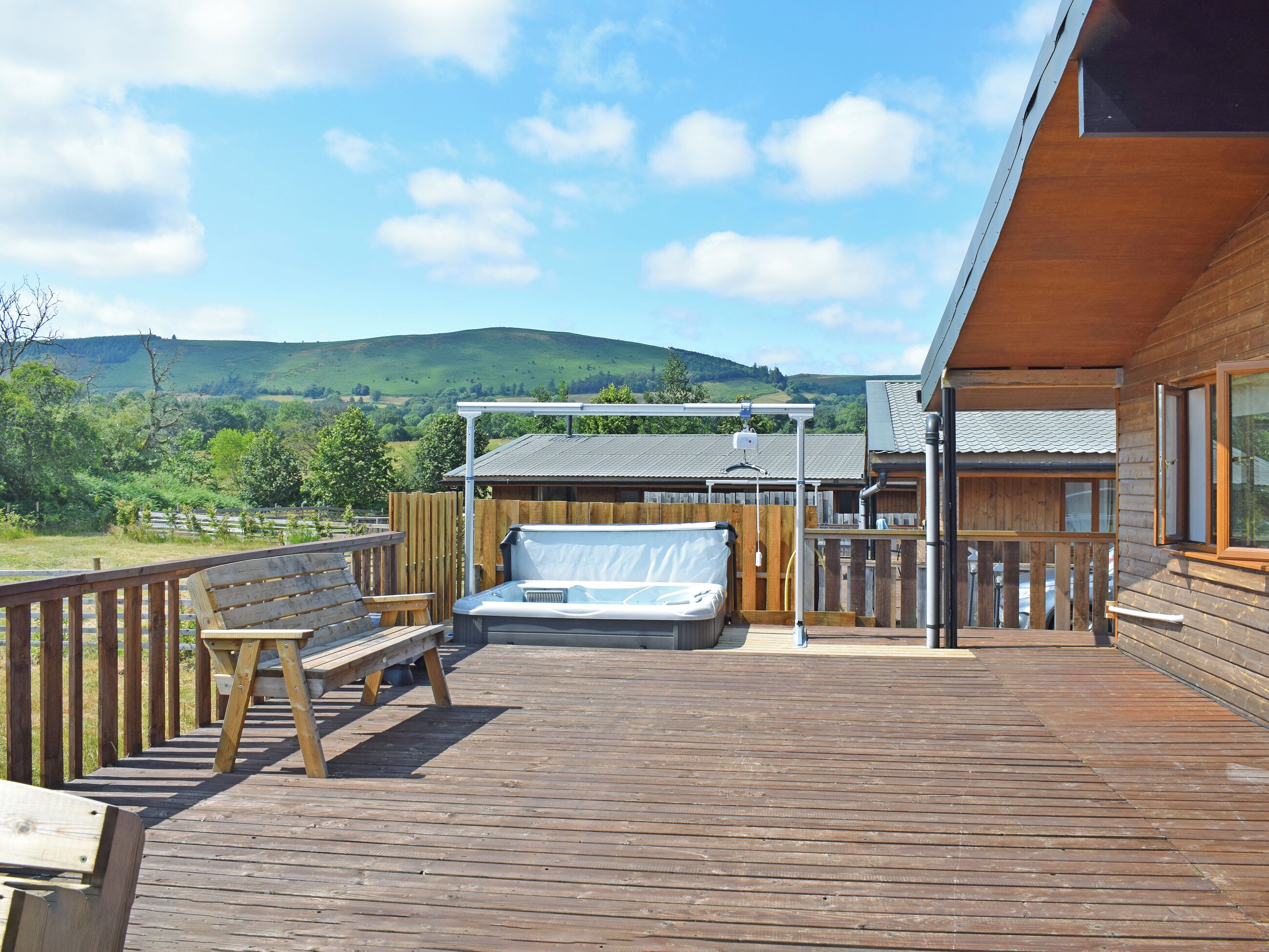A wooden deck with a hot tub, a bench, and a view of a green landscape.